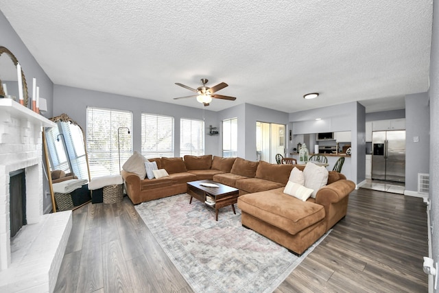 living room with ceiling fan, a fireplace, a textured ceiling, and hardwood / wood-style floors