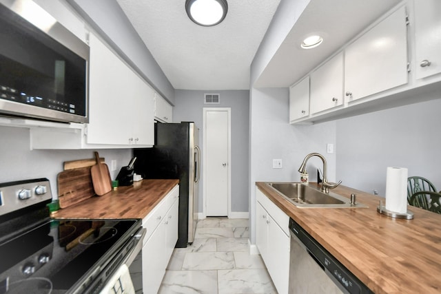 kitchen featuring wood counters, appliances with stainless steel finishes, a textured ceiling, white cabinets, and sink