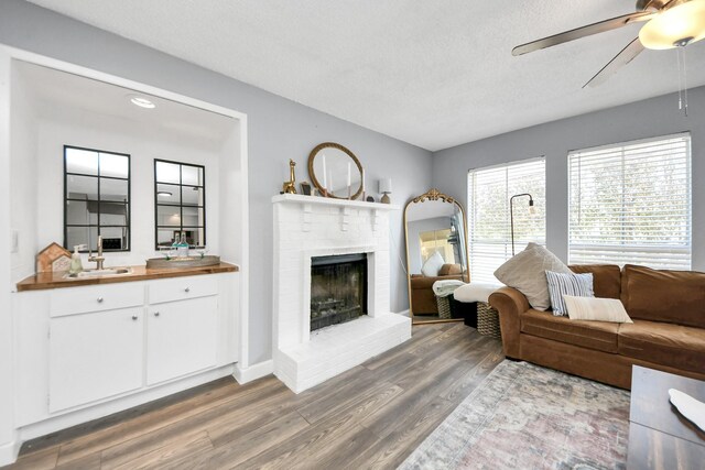 living room featuring ceiling fan, a brick fireplace, hardwood / wood-style floors, sink, and a textured ceiling