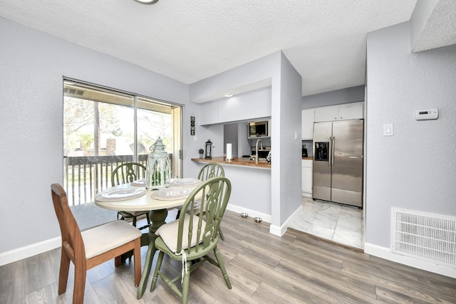 dining space featuring sink, a textured ceiling, and light hardwood / wood-style floors