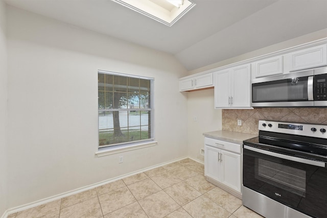 kitchen featuring white cabinets, lofted ceiling with skylight, appliances with stainless steel finishes, and light tile patterned flooring