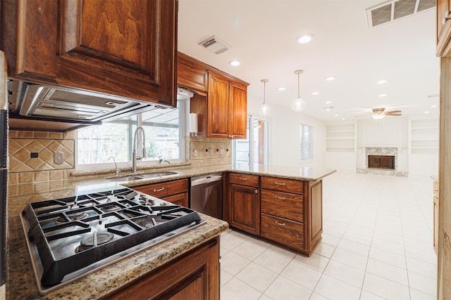 kitchen with appliances with stainless steel finishes, decorative light fixtures, a stone fireplace, sink, and kitchen peninsula