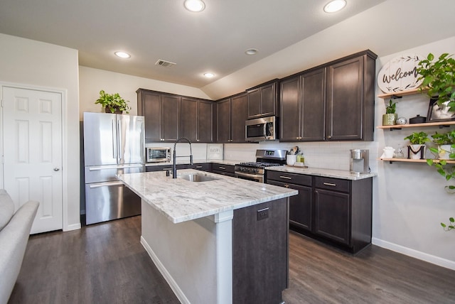 kitchen featuring sink, appliances with stainless steel finishes, an island with sink, dark brown cabinets, and light stone counters