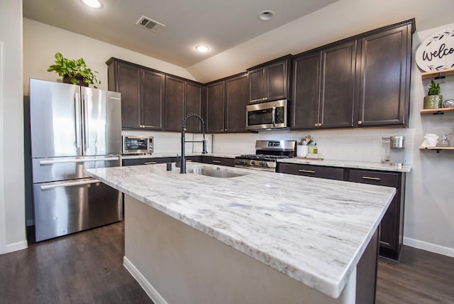 kitchen featuring vaulted ceiling, stainless steel appliances, a center island with sink, and sink