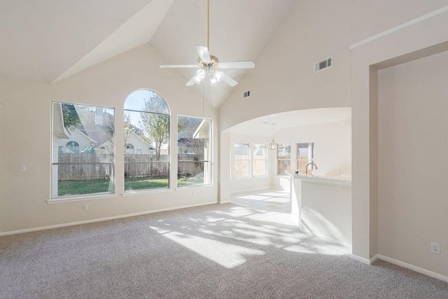 unfurnished living room featuring ceiling fan, a wealth of natural light, light colored carpet, and high vaulted ceiling