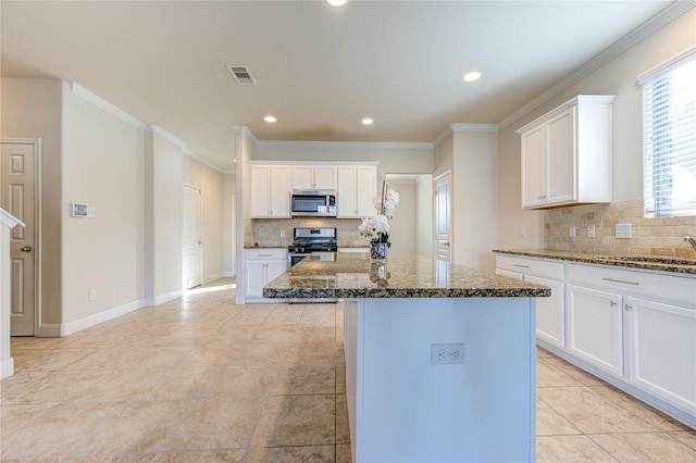 kitchen with white cabinets, a kitchen island, stainless steel appliances, dark stone countertops, and backsplash