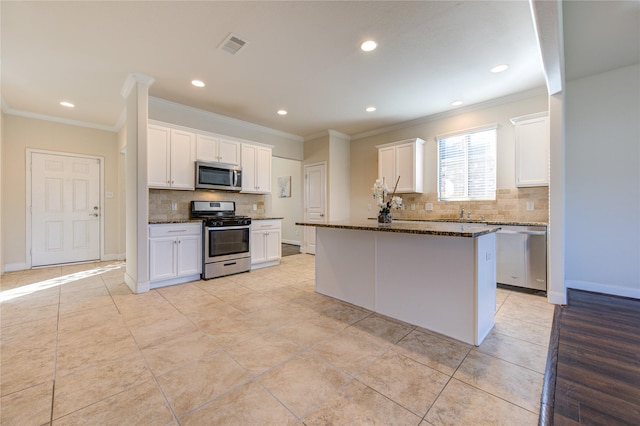 kitchen featuring white cabinets, appliances with stainless steel finishes, a center island, and dark stone counters