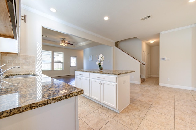 kitchen with white cabinetry, ceiling fan, dark stone countertops, a kitchen island, and sink