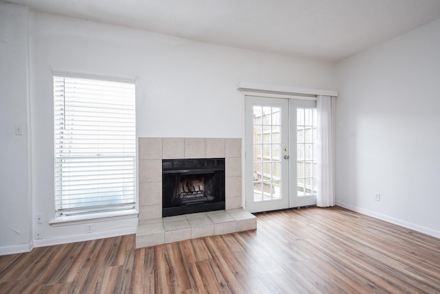 unfurnished living room with light hardwood / wood-style floors, a fireplace, french doors, and a healthy amount of sunlight