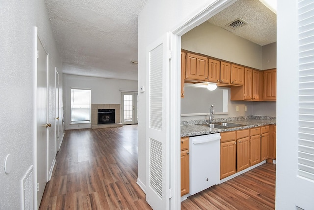 kitchen with hardwood / wood-style floors, white dishwasher, a textured ceiling, a tile fireplace, and sink