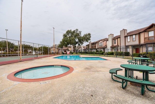 view of swimming pool featuring tennis court and a hot tub