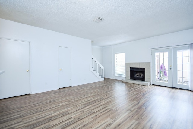 unfurnished living room featuring a tile fireplace, light hardwood / wood-style floors, a wealth of natural light, a textured ceiling, and french doors