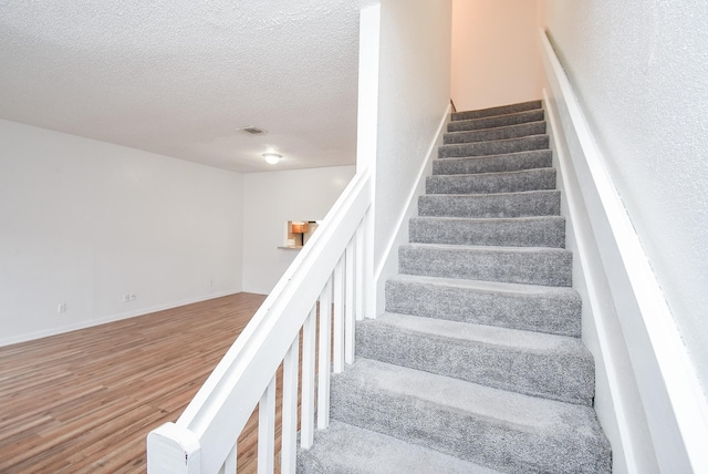 staircase with a textured ceiling and hardwood / wood-style floors