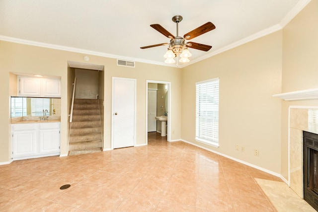 unfurnished living room with a fireplace, sink, ceiling fan, light tile patterned floors, and crown molding