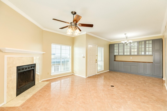 unfurnished living room with light tile patterned floors, ornamental molding, ceiling fan with notable chandelier, and a tiled fireplace