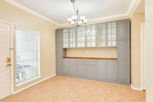 unfurnished dining area featuring a textured ceiling, ornamental molding, a notable chandelier, and light tile patterned flooring