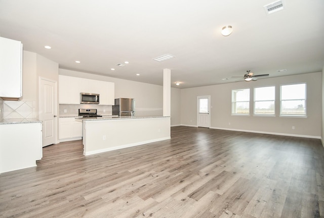 kitchen with ceiling fan, light hardwood / wood-style floors, appliances with stainless steel finishes, an island with sink, and white cabinets