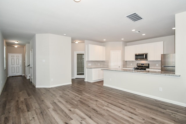 kitchen featuring light stone countertops, hardwood / wood-style floors, white cabinetry, stainless steel appliances, and decorative backsplash