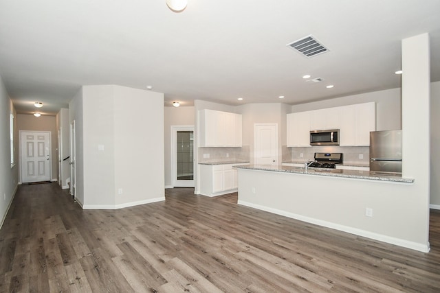 kitchen with hardwood / wood-style floors, white cabinets, appliances with stainless steel finishes, tasteful backsplash, and light stone counters