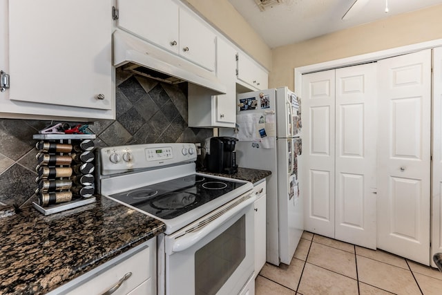 kitchen with light tile patterned floors, white appliances, white cabinets, and dark stone countertops