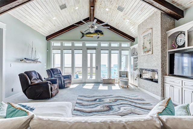 living room with carpet, built in shelves, a stone fireplace, vaulted ceiling with beams, and ceiling fan