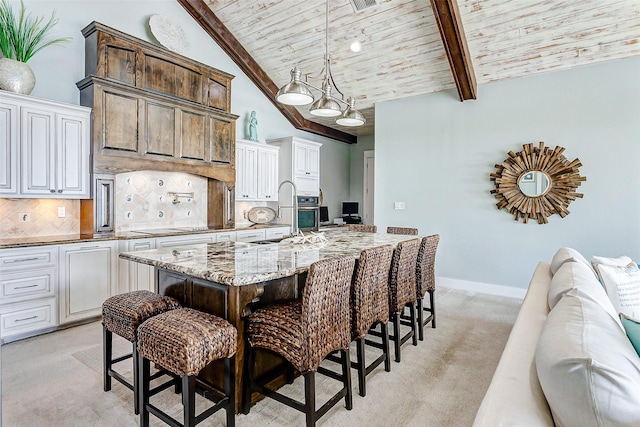 kitchen featuring light carpet, an island with sink, decorative backsplash, wooden ceiling, and beam ceiling