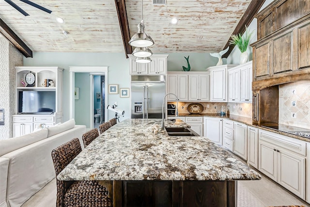 kitchen featuring backsplash, a kitchen island with sink, stainless steel built in refrigerator, a breakfast bar, and sink