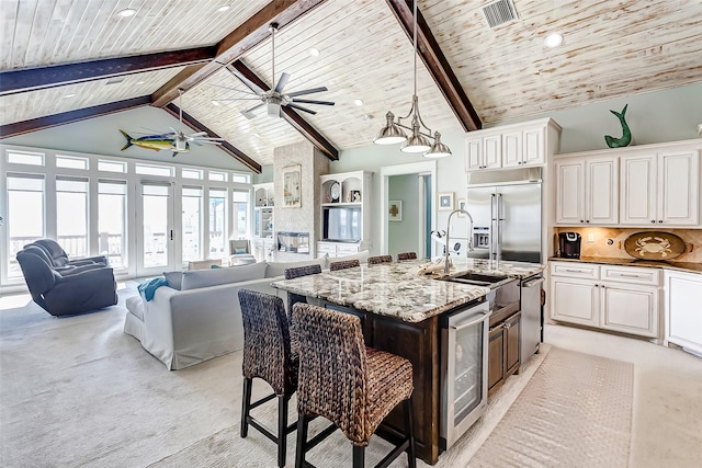 kitchen featuring a kitchen bar, a center island with sink, stainless steel built in fridge, tasteful backsplash, and wine cooler