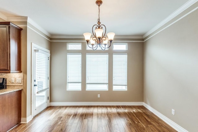 unfurnished dining area with hardwood / wood-style flooring, ornamental molding, and a notable chandelier