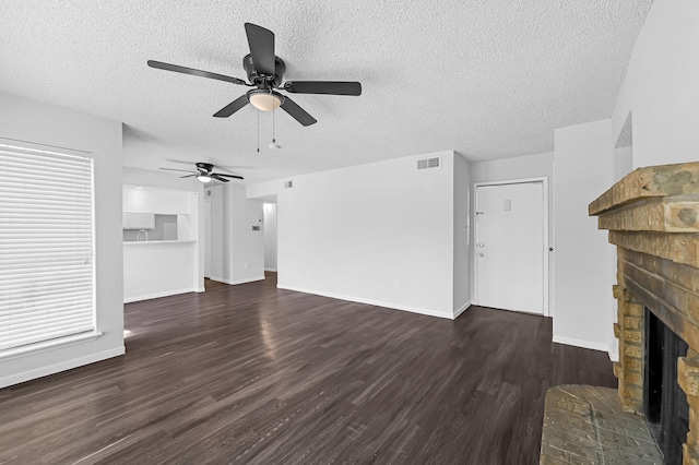 unfurnished living room with ceiling fan, a brick fireplace, a textured ceiling, and dark hardwood / wood-style floors