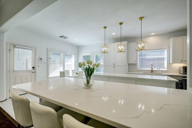 kitchen with tasteful backsplash, sink, white cabinetry, hanging light fixtures, and light stone countertops