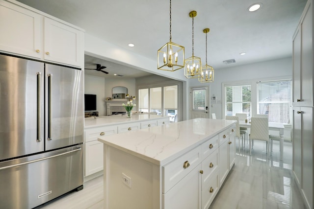 kitchen with ceiling fan with notable chandelier, light stone countertops, white cabinetry, hanging light fixtures, and high end refrigerator