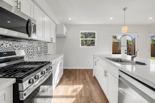 kitchen featuring light stone countertops, pendant lighting, white cabinetry, stainless steel appliances, and light hardwood / wood-style floors