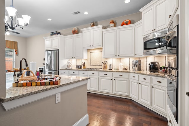 kitchen with appliances with stainless steel finishes, white cabinets, dark hardwood / wood-style flooring, and decorative backsplash