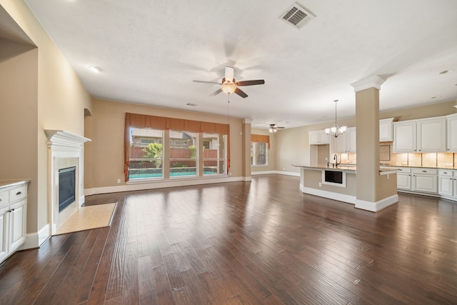 unfurnished living room featuring visible vents, baseboards, a fireplace, and ceiling fan with notable chandelier