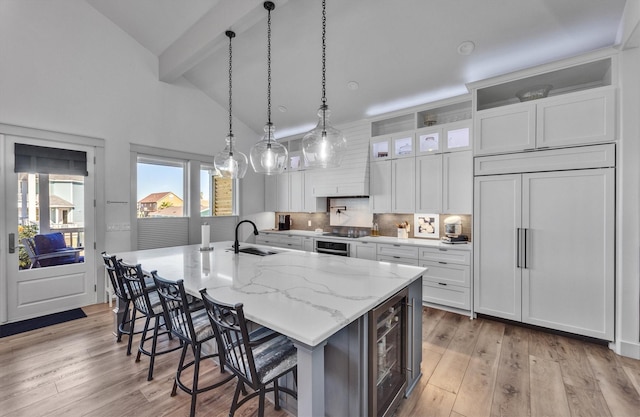 kitchen with a large island, light wood-style flooring, paneled built in refrigerator, white cabinetry, and a sink