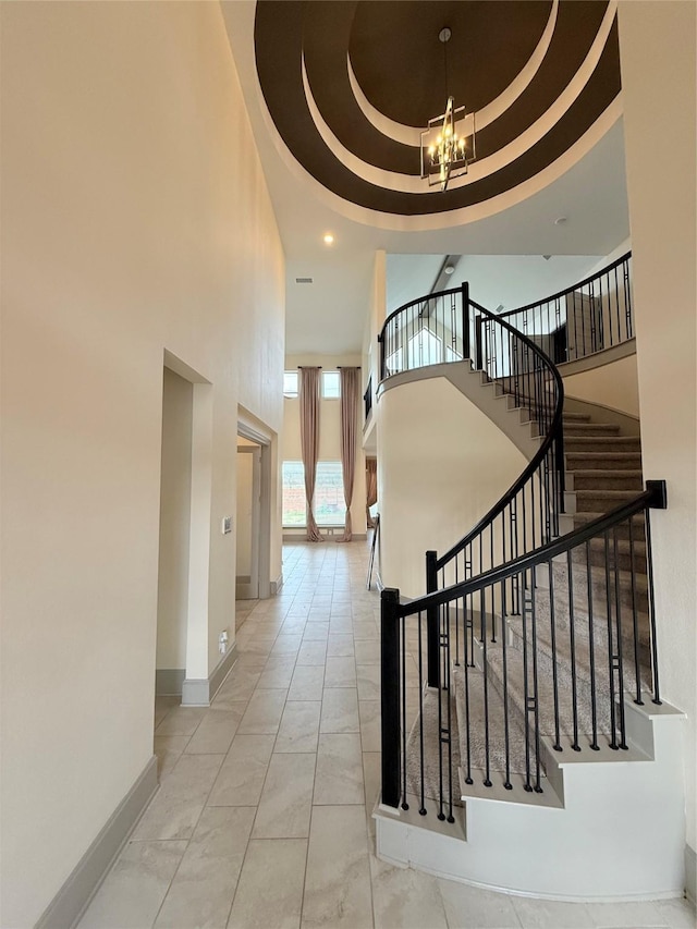 stairs featuring a tray ceiling, a towering ceiling, and an inviting chandelier