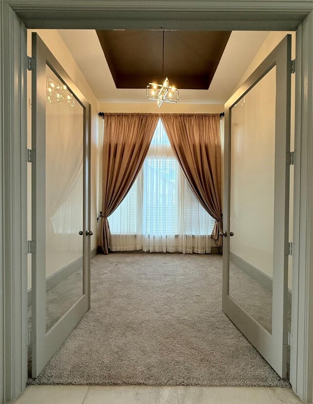 interior space featuring an inviting chandelier, a raised ceiling, and french doors