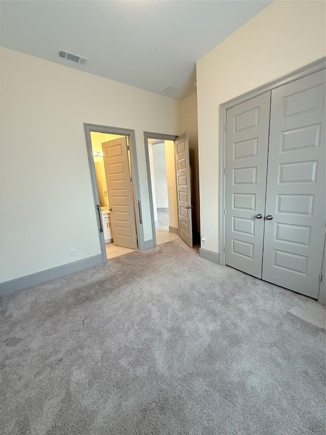 unfurnished bedroom with light carpet, a closet, and ensuite bathroom