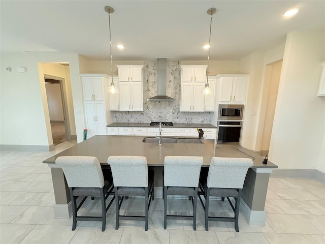 kitchen featuring a large island with sink, white cabinets, appliances with stainless steel finishes, wall chimney range hood, and decorative backsplash