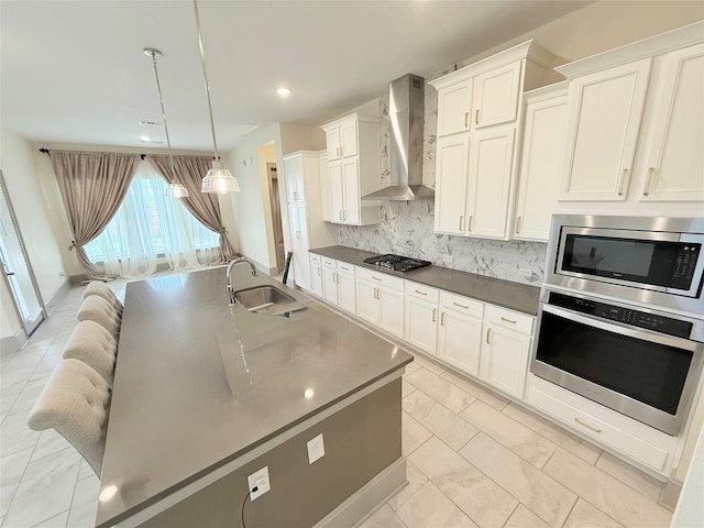 kitchen with decorative light fixtures, backsplash, sink, appliances with stainless steel finishes, and wall chimney exhaust hood