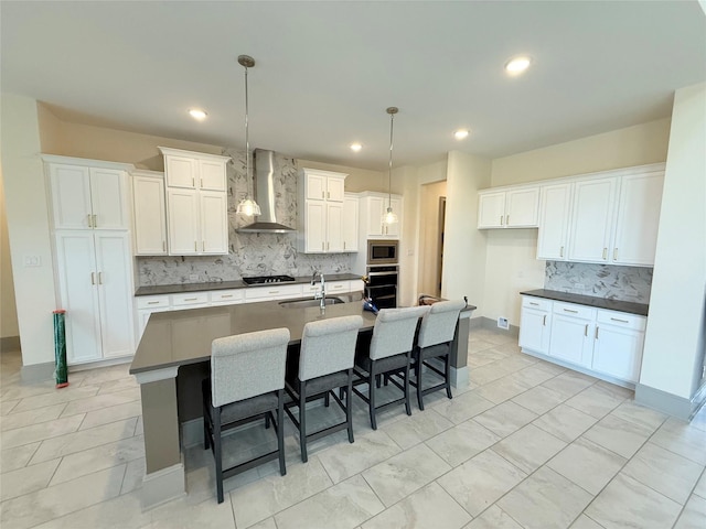 kitchen with pendant lighting, wall chimney exhaust hood, stainless steel appliances, sink, and a kitchen island with sink