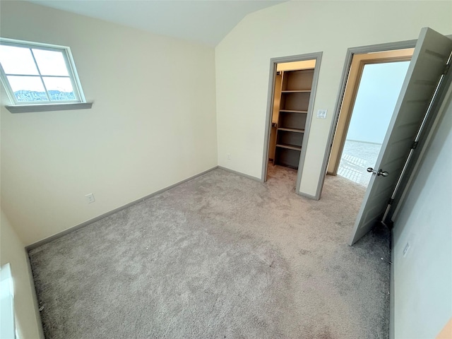 unfurnished bedroom with a spacious closet, light colored carpet, a closet, and lofted ceiling