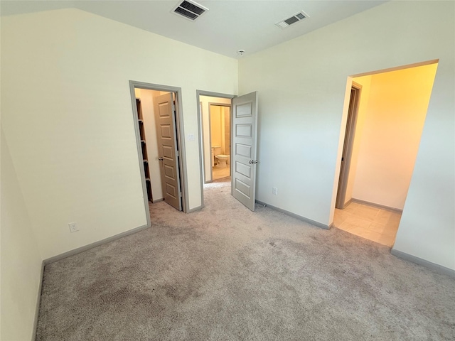 unfurnished bedroom featuring light colored carpet, ensuite bath, a walk in closet, and vaulted ceiling