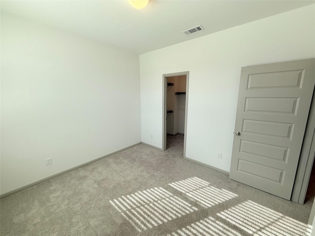 unfurnished bedroom featuring a walk in closet, a closet, and light carpet