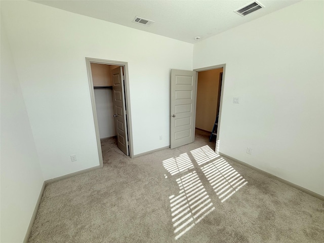 unfurnished bedroom with a walk in closet, a closet, and light colored carpet