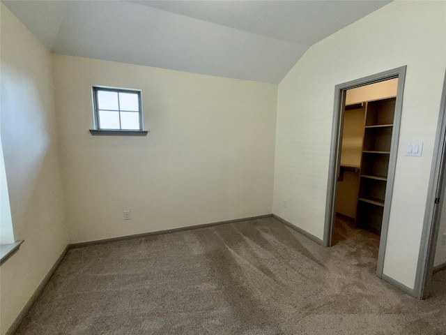 unfurnished bedroom featuring lofted ceiling, a closet, baseboards, carpet floors, and a walk in closet