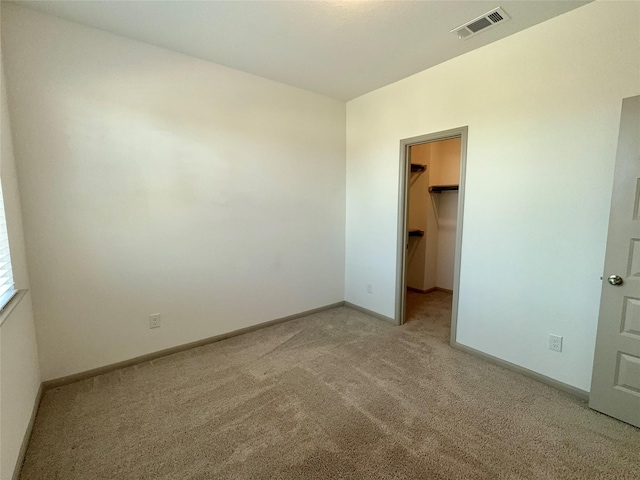 unfurnished bedroom featuring a closet, visible vents, light carpet, baseboards, and a spacious closet