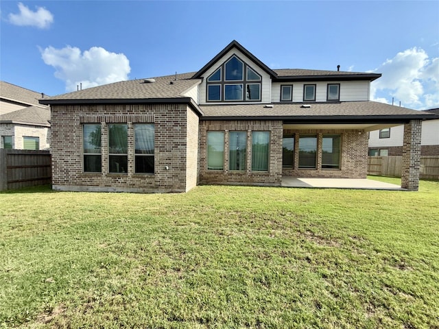 back of house with a yard, brick siding, fence, a shingled roof, and a patio