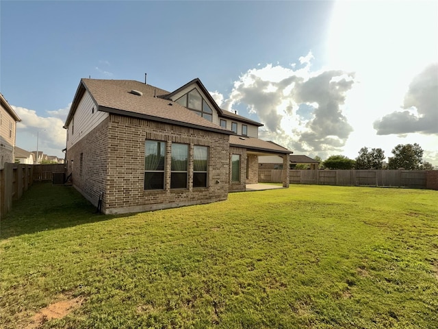 rear view of property featuring a yard, brick siding, and a fenced backyard